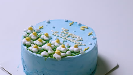 acercarse a un pastel de cumpleaños cubierto con crema de mantequilla azul, y decorado con flores blancas de punta amarilla