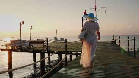 A-Woman-In-A-Pair-And-Hat-Walks-On-The-Pier-In-The-Early-Morning-Breathes-In-The-Fresh-Air-Steadicam