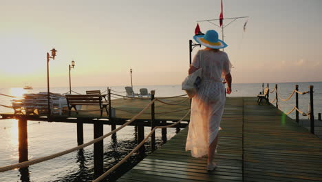 a woman in a pair and hat walks on the pier in the early morning breathes in the fresh air steadicam