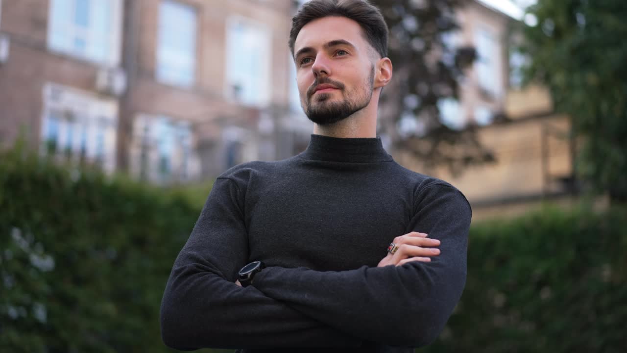 Medium shot of confident stylish man with crossed hands looking away standing on city street. Handsome brunette Caucasian young businessman downtown. Success and lifestyle.