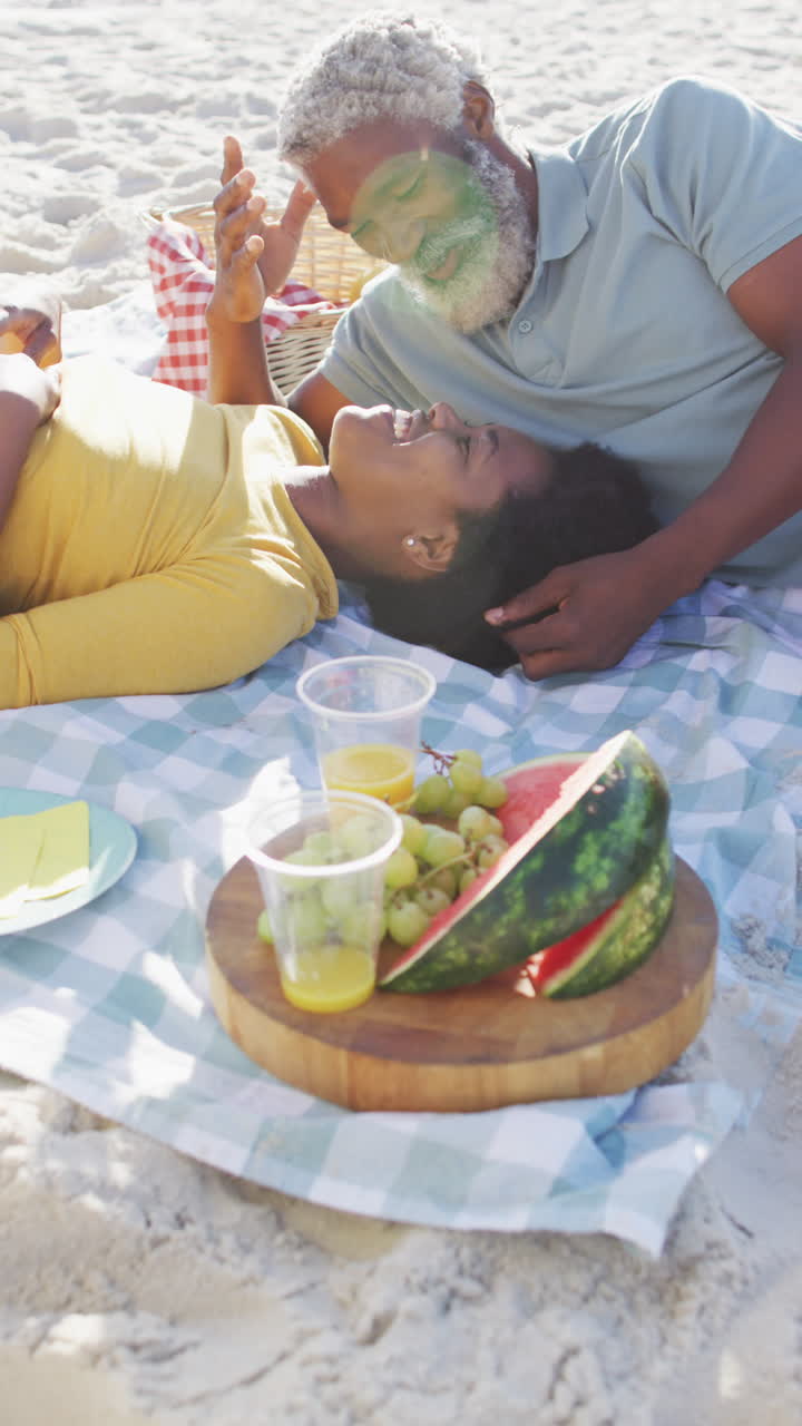 video vertical de un anciano afroamericano y una mujer haciendo picnic en la playa