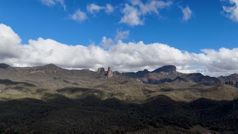 drone footage pans across rugged volcanic mountains under scattered clouds and bright daylight in warrumbungle national park, highlighting dramatic shadows and natural textures