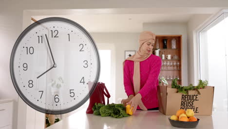 biracial woman in hijab holding vegetables in kitchen over clock