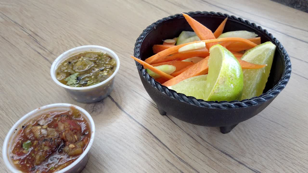 Close up of Mexican pickled vegetables with carrot, cucumber, lime, and green salsa on wooden table