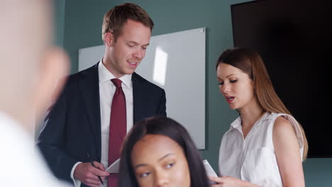 young businessman and businesswoman watching group meeting around table at graduate recruitment assessment day