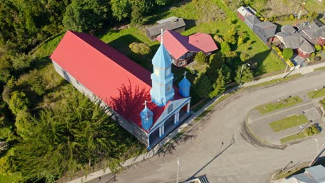 vibrant blue patrimony church in tenaun with a red roof in chiloé, chile, on a sunny day, aerial view