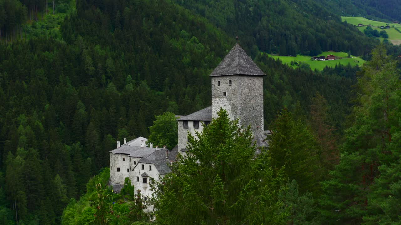 Stoupající letecký záběr nad starobylým kamenným hradem obklopeným zelenými stromy