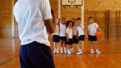 Schoolboy-clicking-photo-with-mobile-phone-of-his-friends-in-basketball-court-at-school-4k