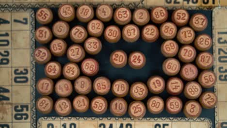 cinematic close-up smooth shot from above of a pile of bingo wooden barrels in a square, woody figures, old numbers background, vintage board game, slow motion 120 fps commercial video pan left