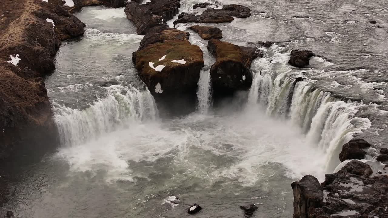 Scenic aerial view of Goðafoss waterfall in northern Iceland, with its iconic semi-circular shape and powerful river flow through basalt formations
