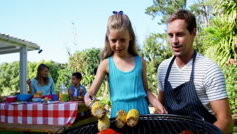 padre e hija asando salchichas y maíz en la barbacoa