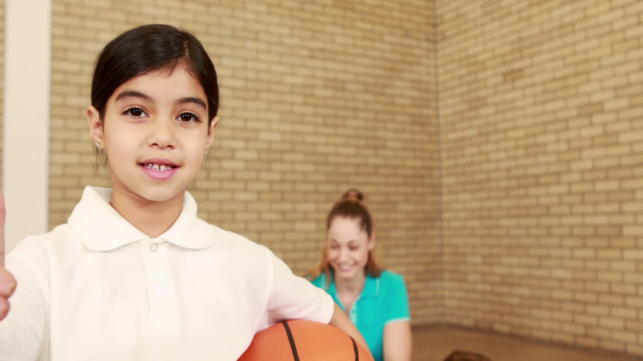 chica sonriente con los pulgares hacia arriba sosteniendo el baloncesto