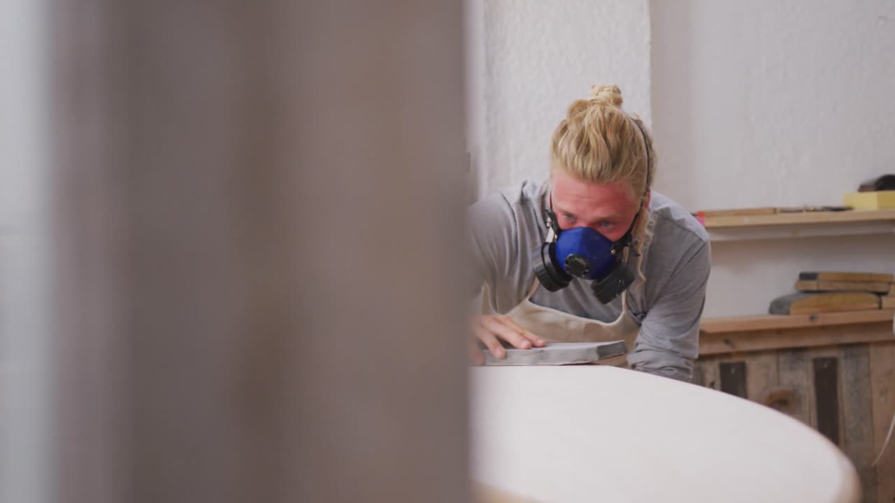 кавказский мужчина-производитель доски для серфинга в маске и полирует доску для серфинга