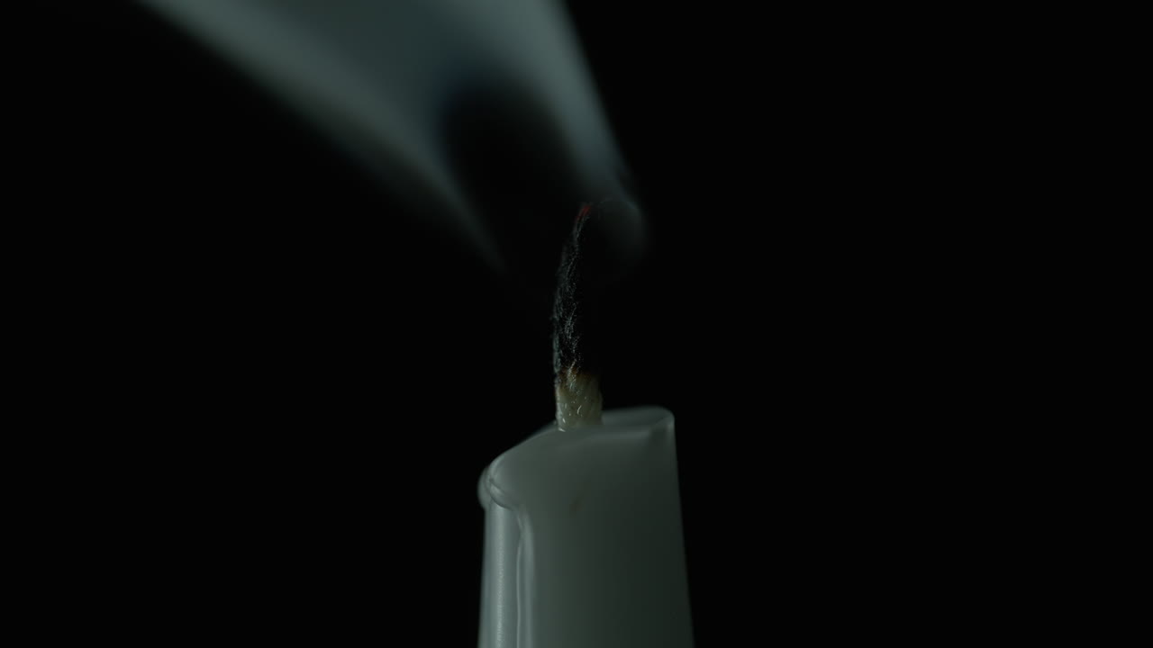 Air blowing out candle flame dark studio closeup shot. Taper wax fire on black