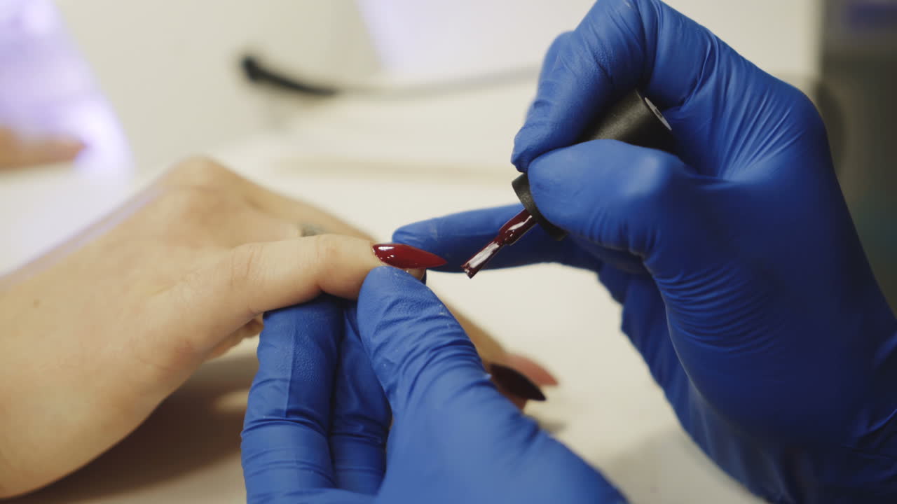Process of doing manicure in the spa salon. Beautician applying red nail polish on the nails in the beauty salon. Concept of hand care.
