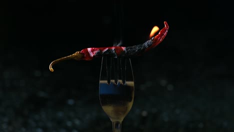 Hot-red-chili-pepper-on-a-fork-in-flames-on-a-black-background