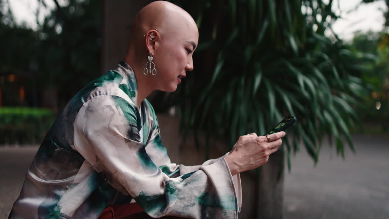 Donna con la testa rasata che usa il telefono al parco