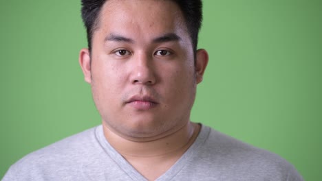 young handsome overweight asian man against green background