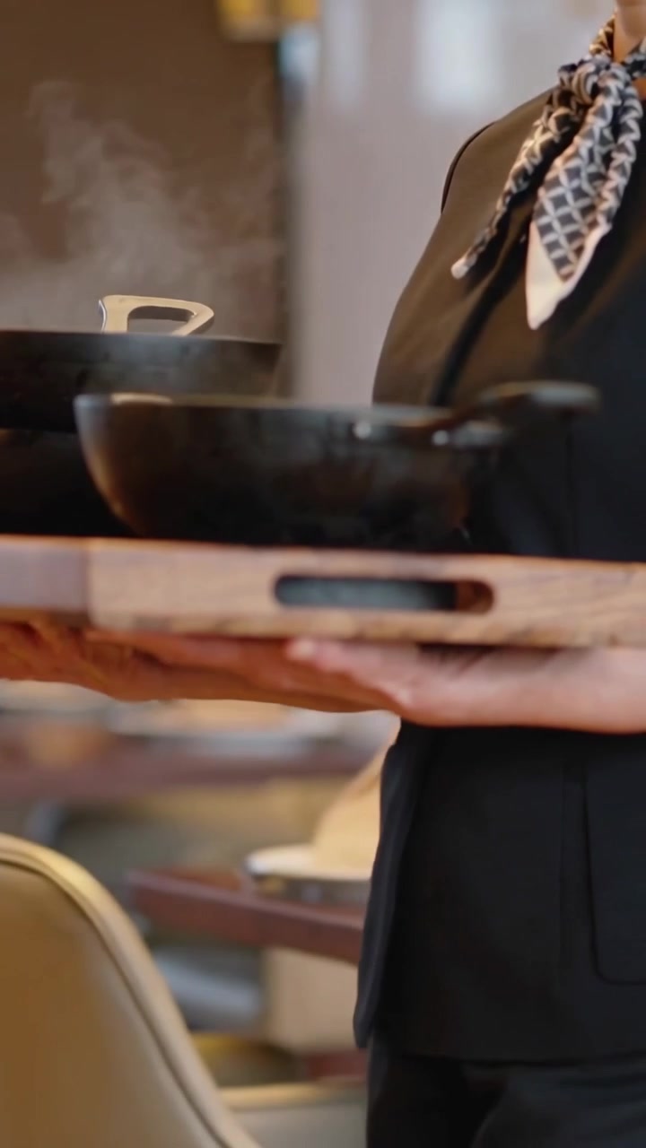 Video verticale: Un cameriere con la sciarpa cammina tenendo un vassoio di padelle di ferro, passando davanti al ristorante dopo che l'ordine è pronto.