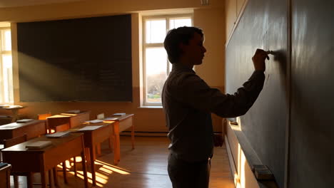 student writing on a blackboard in a sunlit classroom