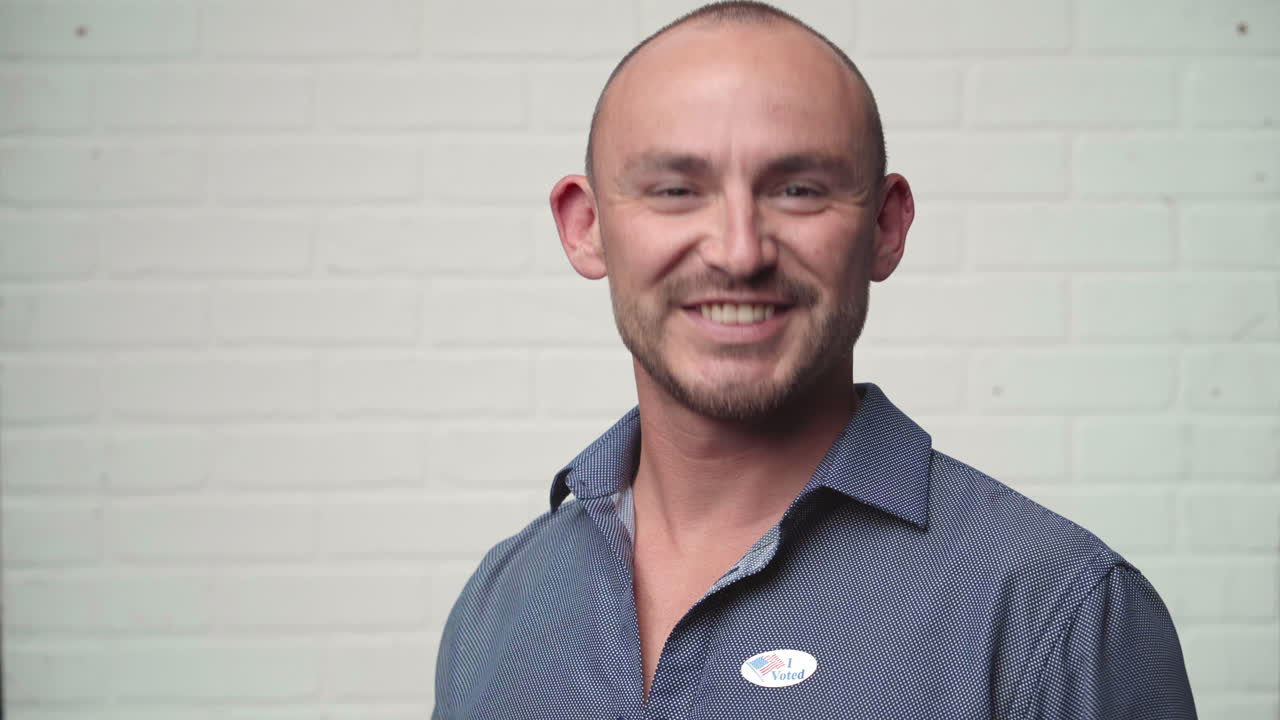 el hombre entra y pone una pegatina de votación en la camisa, sonriendo con orgullo.