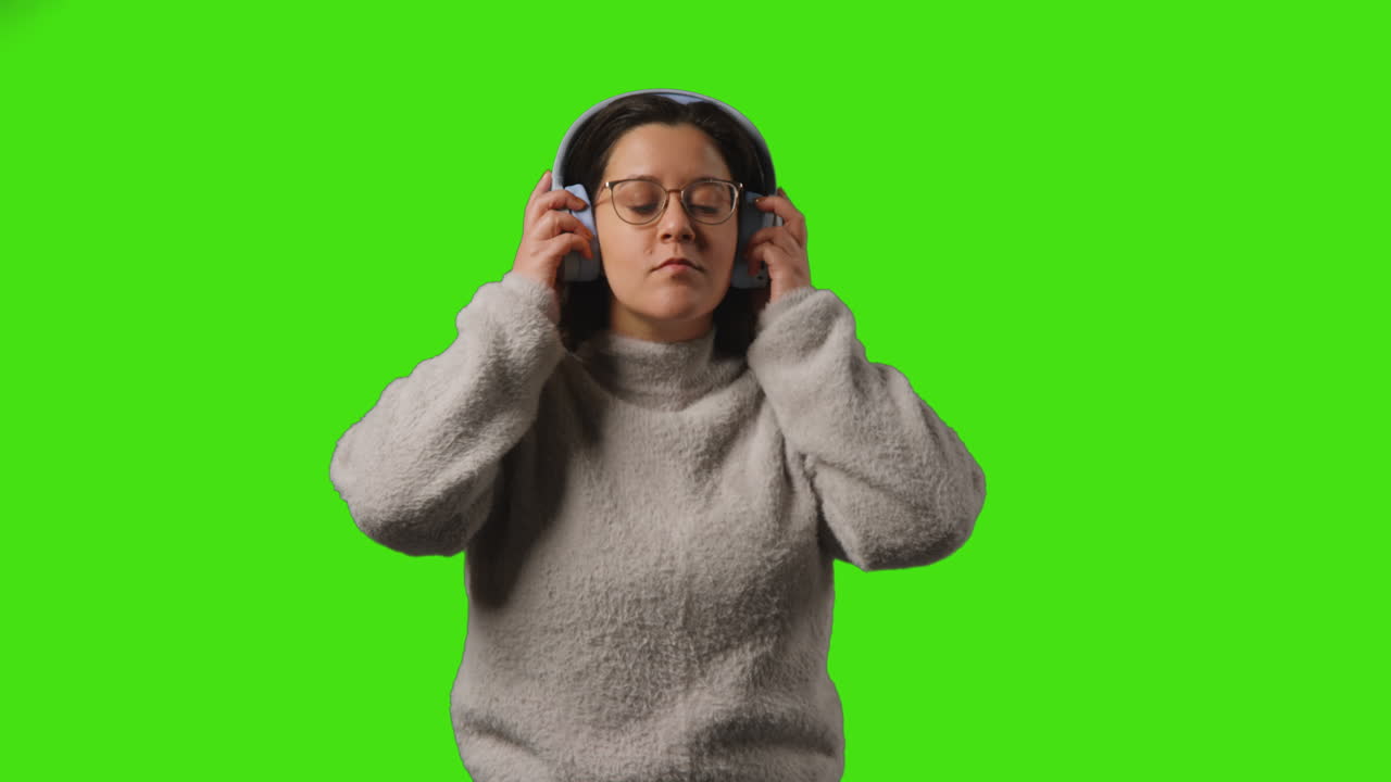 joven con auriculares inalámbricos transmitiendo música desde un teléfono móvil contra la pantalla verde del estudio