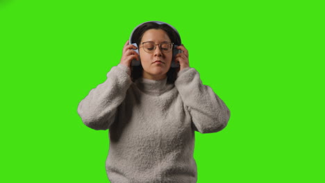 young woman wearing wireless headphones streaming music from mobile phone against studio green screen