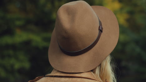 primer plano de la vista trasera de la hermosa chica rubia con un sombrero girando la cabeza y sonriendo a la cámara en otoño