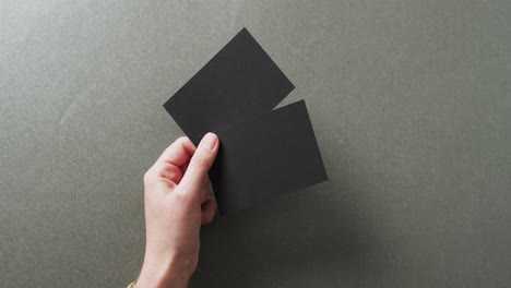 hand of caucasian woman holding two black business cards on grey background, copy space, slow motion