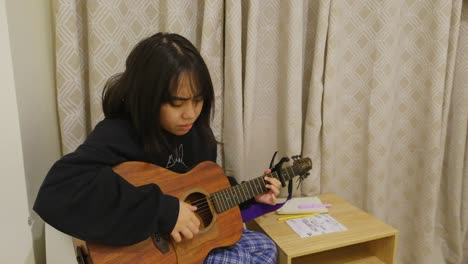 Chica-Asiática-Seria-Tocando-La-Guitarra-Acústica-En-La-Habitación