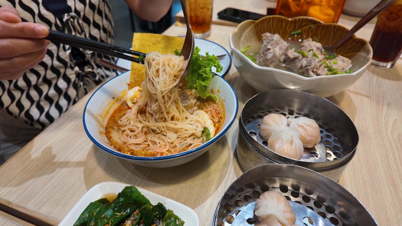 Seseorang mengangkat mi pedas Thailand dengan sumpit di samping dim sum dan sup babi di Bangkok