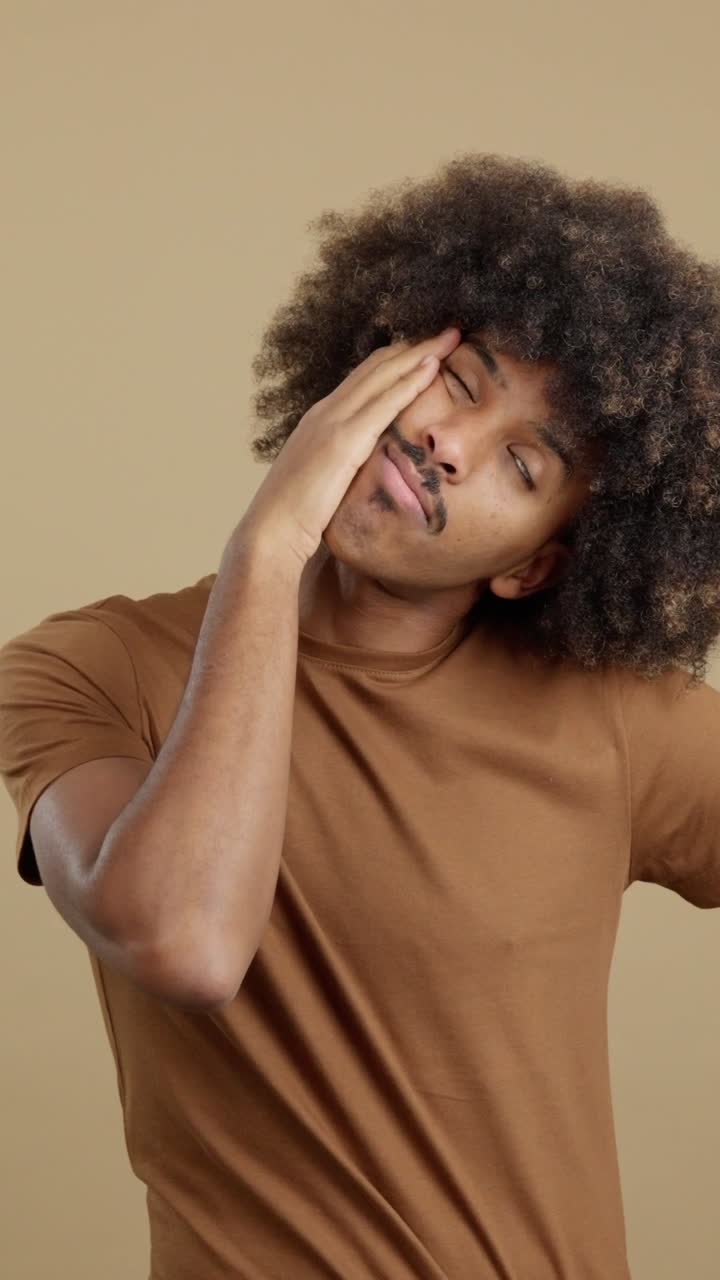 A man with curly hair and a mustache posing in a brown t-shirt
