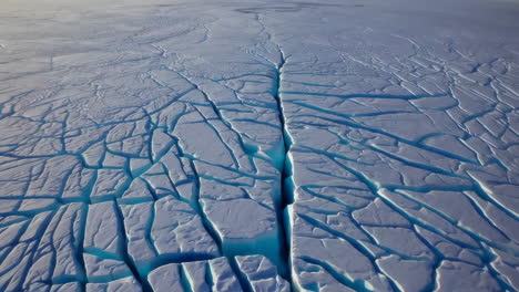 aerial view of cracked polar ice with turquoise water fissures