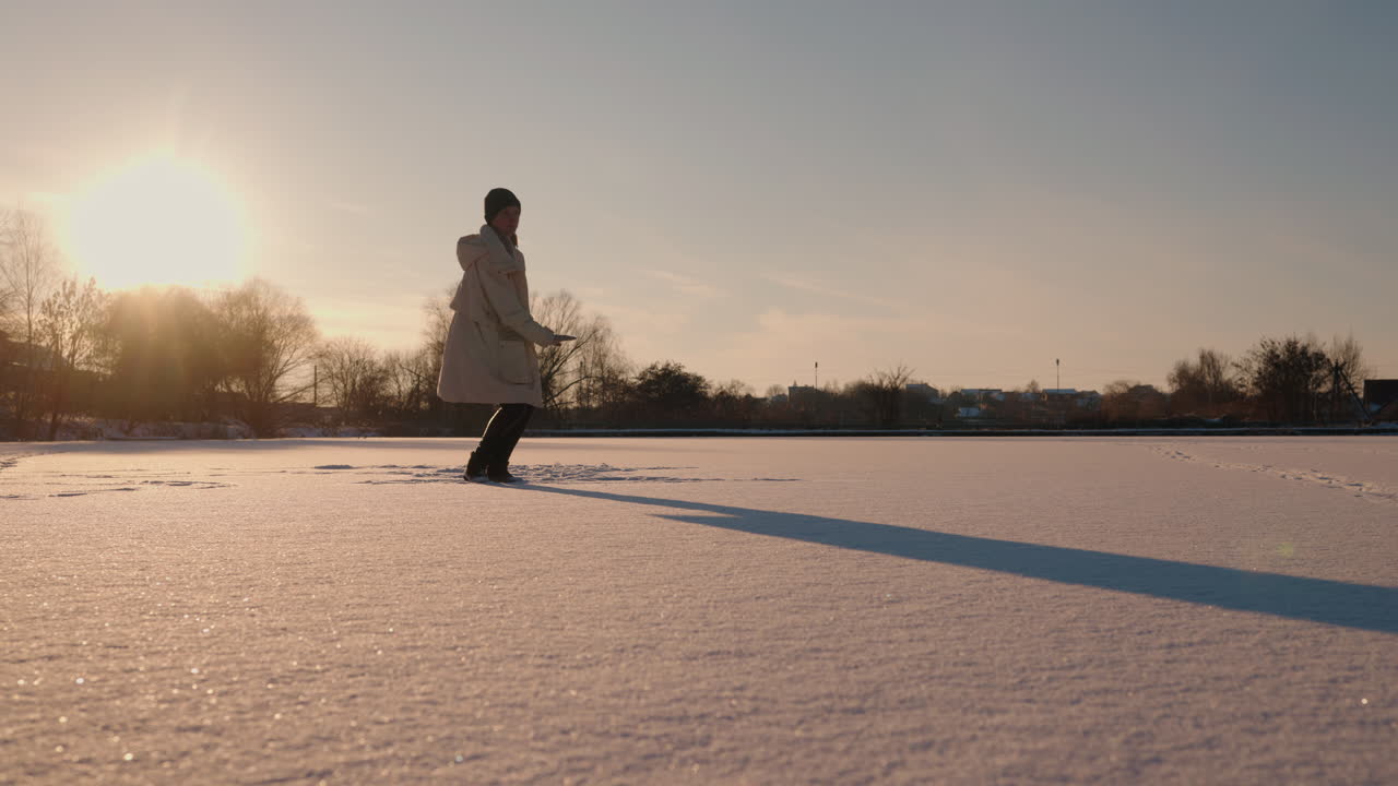 해가 지는 동안 얼어붙은 호수 위를 고 있는 여자