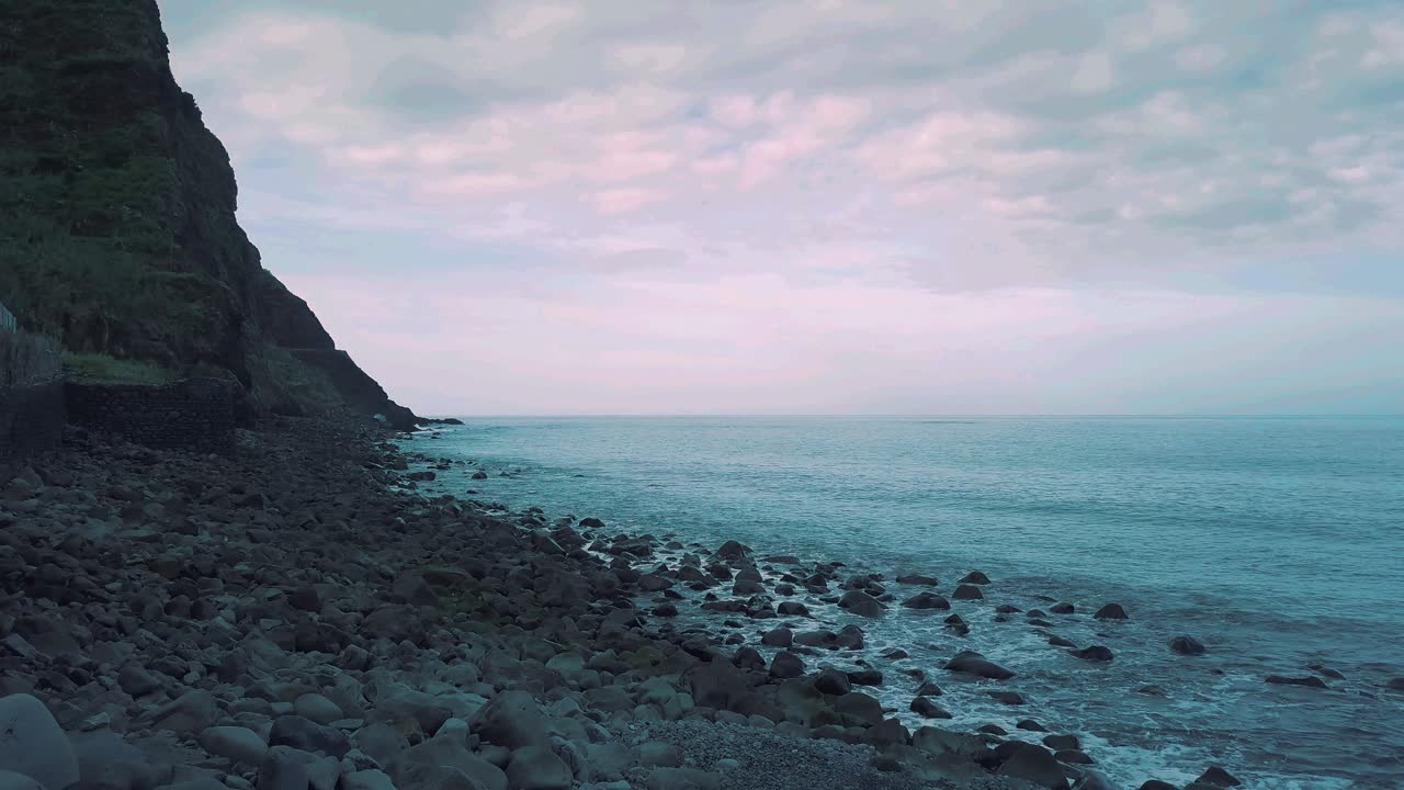 해변에서 조약돌 바위를 드러내는 쌓인 돌을 지나 앞으로 날아가는 일출의 화산 바다 풍경, 하늘 - 대서양 마데이라 섬 풍경 hd 시네 등급 왼쪽에서 오른쪽으로