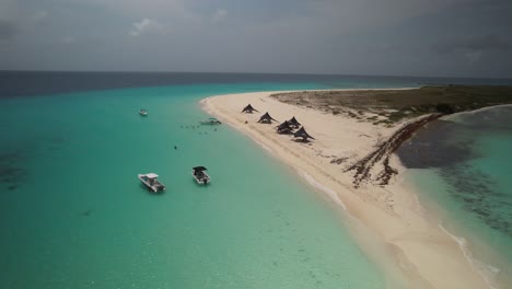 Drone-shot-of-people-enjoying-a-pristine-sandy-beach-with-turquoise-water-and-tents-under-a-cloudy-sky