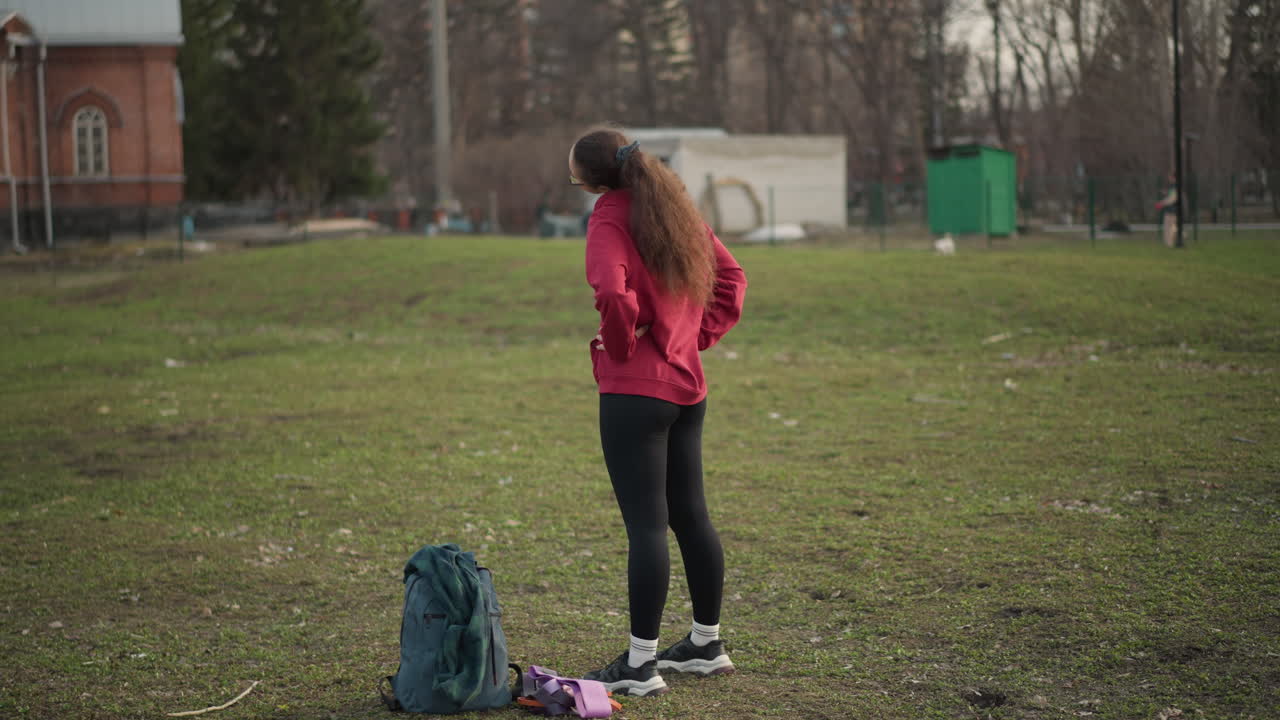 Women In Park, Young Woman Observes Peaceful Scenery, Girl With Backpack Looks Over Calm Park Landscape, Youthful Female In Red Hoodie Pauses Thoughtfully Amid Serene Park Surroundings