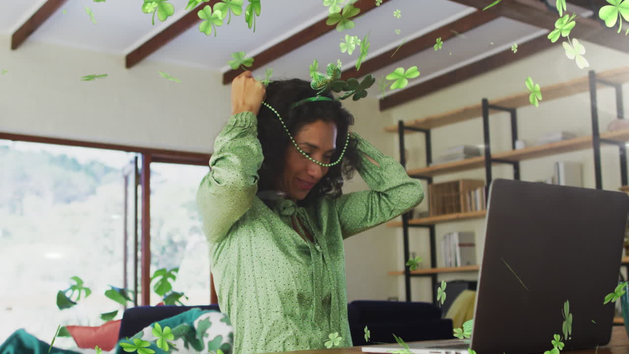 Animation of shamrocks falling and biracial woman in shamrock glasses celebrating st patrick's day