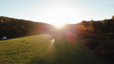 Epische-Drohnenaufnahme-Aus-Der-Luft-Von-Sonnenstrahlen-Auf-Einer-Wiese,-Umgeben-Von-Wald-Bei-Sonnenuntergang-5