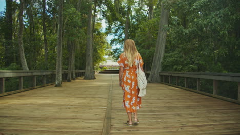 Toma-En-Cámara-Lenta-De-Una-Hermosa-Chica-Rubia-Con-Un-Vestido-Colorido-Descubriendo-Florida-Springs-Chica-Caminando-Disfrutando-Del-Pintoresco-Entorno-Del-Parque-Verde