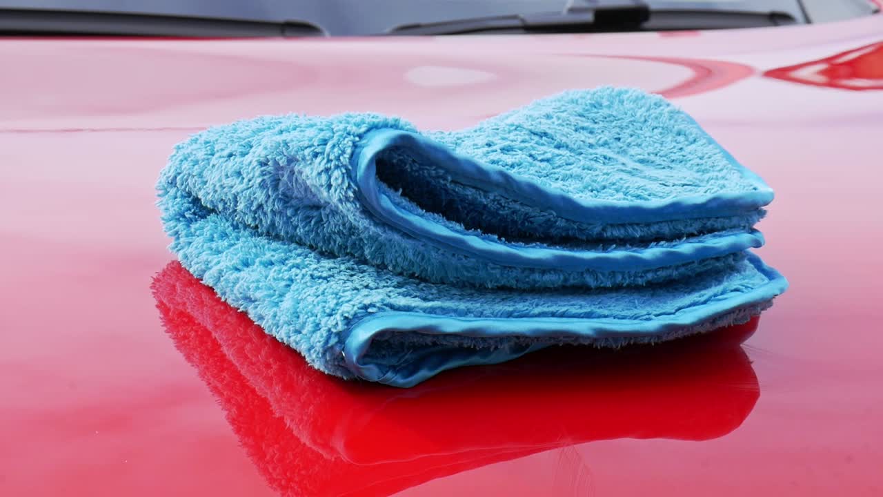 Folded super soft blue microfibre cloth with silk edges on a red car bonnet hood - extreme close up