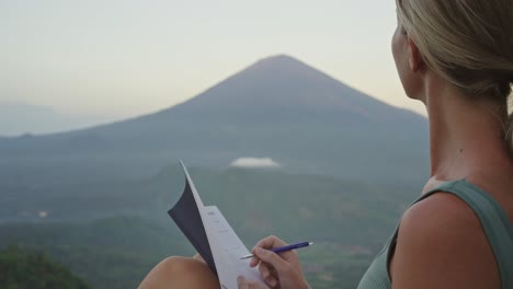 mujer atractiva escribiendo en un cuaderno mientras mira el inspirador paisaje montañoso