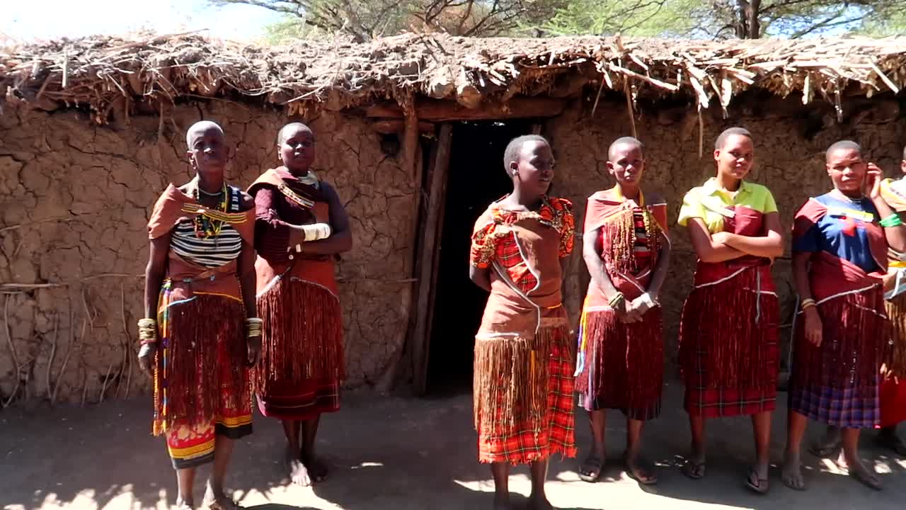 Datoga tribe women in traditional colorful clothing waiting to welcome tourists. Panning right