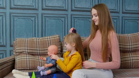 Mujer-Cuidando-Y-Cepillando-El-Cabello-De-Su-Hermana-Pequeña-En-La-Sala-De-Estar,-Niña-Jugando-Con-Una-Muñeca-De-Juguete