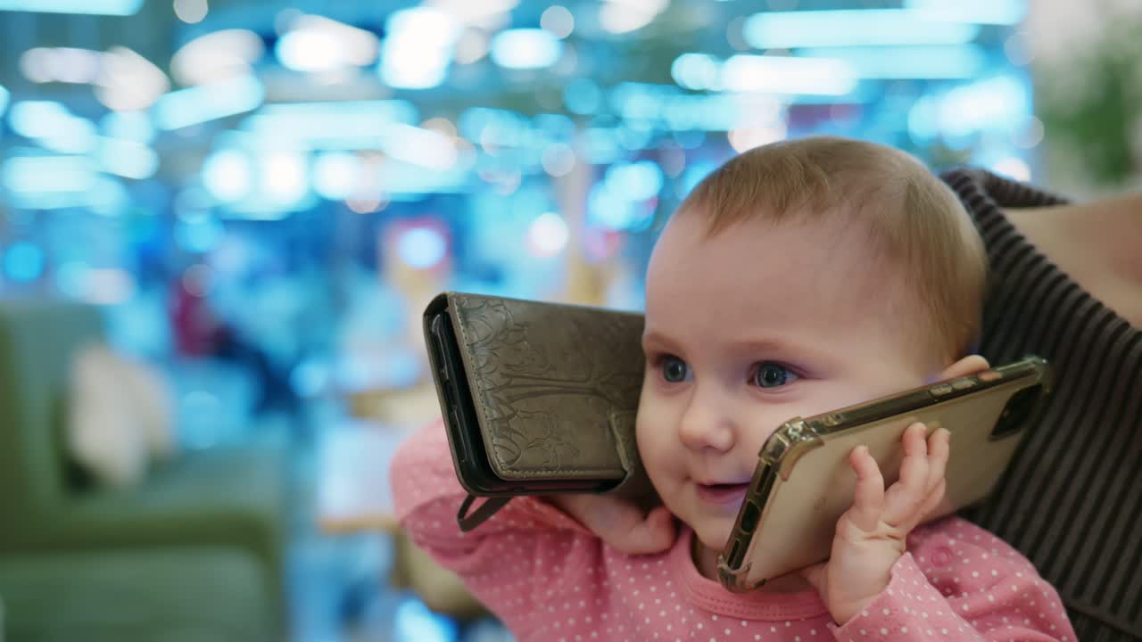 Bebé adorable imitando hablar en dos teléfonos inteligentes