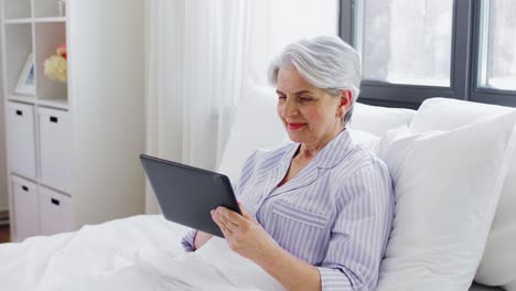 Senior-Woman-with-Tablet-Pc-in-Bed-at-Home-Bedroom.technology,-old-age-and-people-concept--senior-woman-with-tablet-pc-computer-in-bed-at-home-bedroom