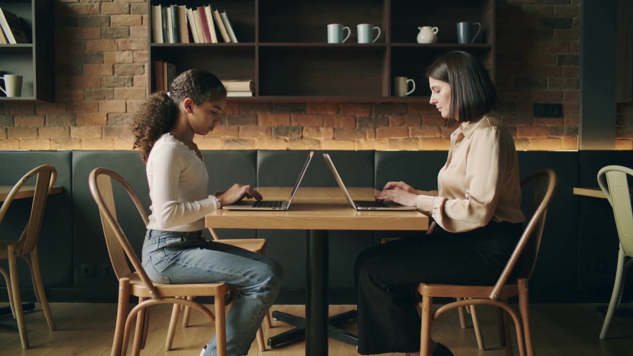 Studerende taster, vejleder når studiesessionen starter, laptops på café, iført lang top og beige bluse.