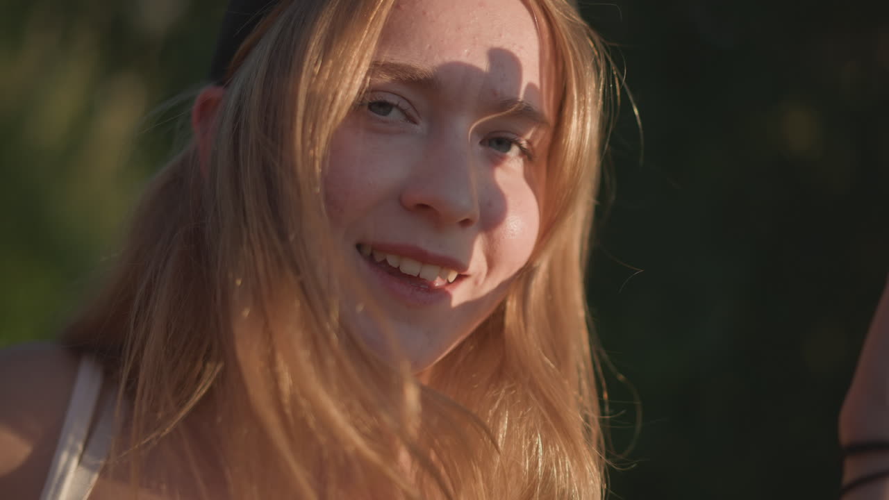 golden hour girl smiling in park, candid headshots showing laughter and hand gestures, beanie hat and sunlit hair, freckles and soft skin tones, relaxed friend vibe and casual conversation, joyful