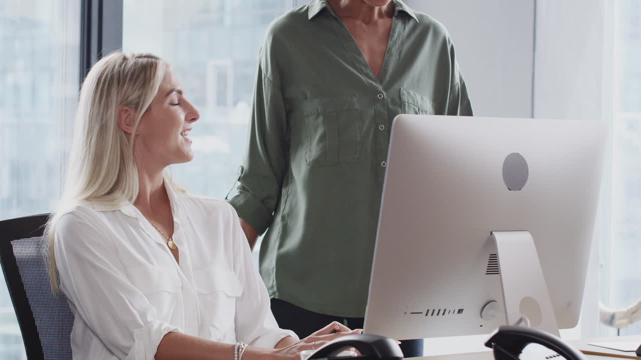 밀레니얼 흑인 여성이 책상에서 여성 동료와 대화를 나누고 나서 걸어가서 가만히 있습니다.