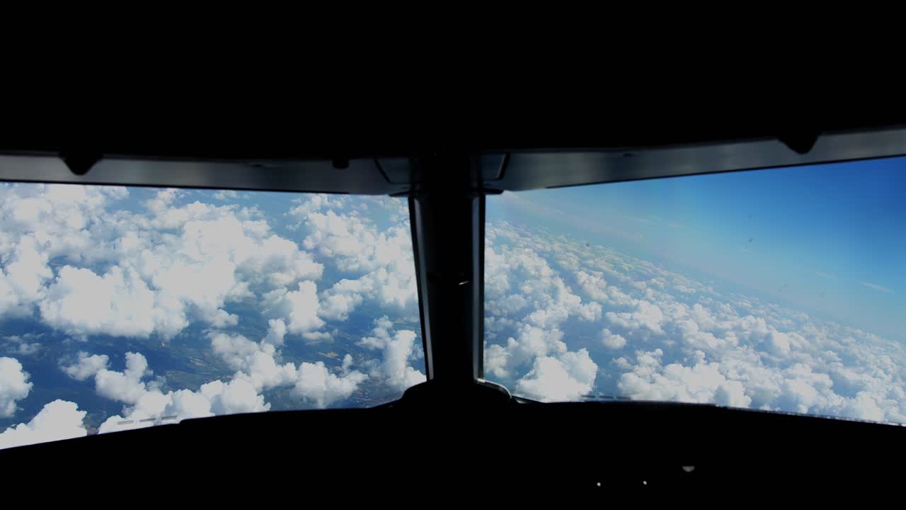 Toma cinematográfica de ángulo alto desde la cabina. Las imágenes muestran un vasto horizonte de nubes blancas y esponjosas bajo un cielo azul claro, con la silueta del panel de instrumentos y la parte superior.
